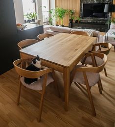 a black and white cat sitting at a table in a living room with wooden chairs