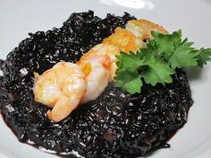 a white plate topped with black rice and shrimp on top of it, garnished with parsley