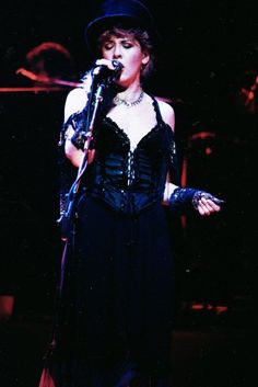 a woman in a black dress and hat singing into a microphone