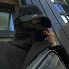 a man wearing a black hat and sunglasses talking on a cell phone while holding a bag