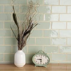 a clock sitting on top of a wooden table next to a vase filled with dry grass