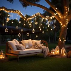 a couch sitting under a tree with lights hanging from it's branches and lanterns