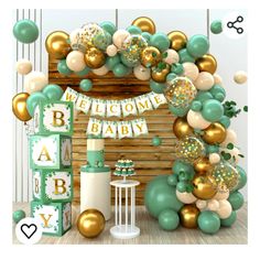 a welcome baby sign and balloons in front of a wooden wall with green, gold and white decorations