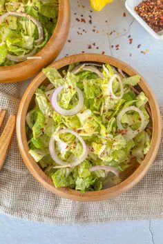 two wooden bowls filled with lettuce and onions next to some seasoning on the table