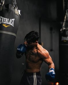 a shirtless man wearing boxing gloves and punching mitts in a black gym room