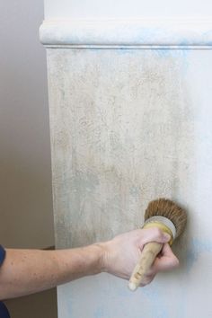 a person with a brush in their hand on a wall painted white and gray color