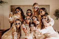 a group of women in white dresses and sunglasses holding up wine glasses while sitting on a couch