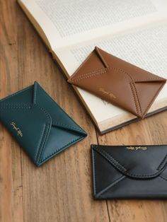 three wallets sitting on top of a wooden table next to an open book and envelope