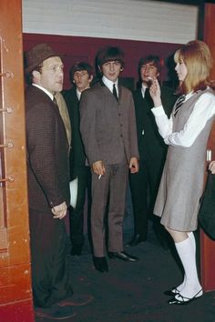 a group of people standing around each other in front of a door with one person talking on the phone