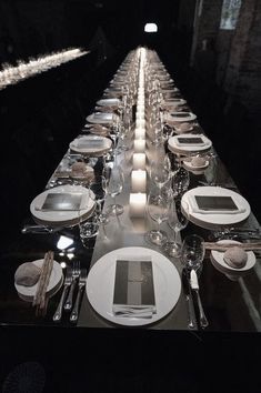 a long table is set with plates, silverware and candles for an elegant dinner