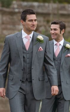 two men in grey suits and pink ties are walking down the street with other people