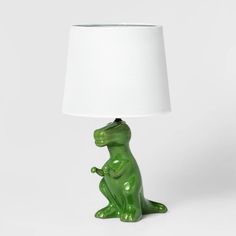 a green dinosaur lamp sitting on top of a table next to a white lampshade