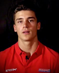 a young man in a red shirt is looking at the camera and has an intense look on his face