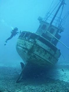 an old ship in the middle of the ocean with two scuba divers looking on from below