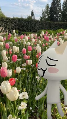 a white cat statue standing in a field of tulips