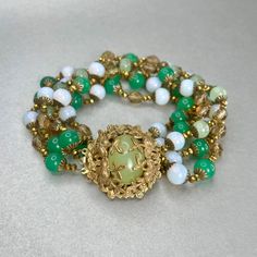 "Vintage Miriam Haskell Green Bracelet, Gold tone Multi Strand Jade Glass Bead Bracelet, Midcentury Collectible Signed Jewelry, Gift for Her. Era: Around 1950- 1951. Designer Signed: Miriam Haskell. Measurements: - Length Around Wrist : 8 1/2\" - Width: 1 1/2\" Details: -Metal Color: Gold - Embellishments: Gold Tone Plating, Pendant with Light Green Glass Stone in the middle. Five gleaming Strands of small Round Beads that are linked in-between by tiny Gold beads strands. Glass Beads: imitation Elegant Multi-strand Bracelet With Faceted Beads, Elegant Multi-strand Beaded Bracelets With Spacer Beads, Elegant Multi-strand Polished Beaded Bracelets, Vintage Adjustable Polished Beads Jewelry, Vintage Faceted Beads Bracelet, Adjustable Vintage Jewelry With Polished Beads, Vintage Bracelets With Spacer Round Beads, Vintage Adjustable Beaded Bracelets With Round Beads, Vintage Bracelets With Round Spacer Beads