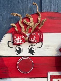 a red and white wooden reindeer head hanging on the side of a blue door with rope