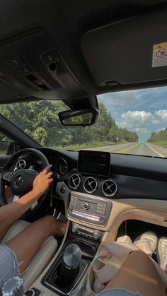 a person driving a car on a road with trees in the background and clouds in the sky