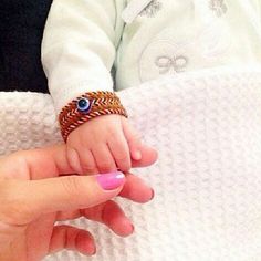 a woman holding a baby's hand while wearing a knitted bracelet with an evil eye on it