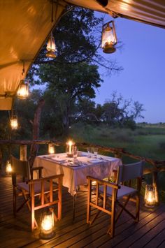 an outdoor dining area with candles lit on the table and chairs, overlooking a grassy field