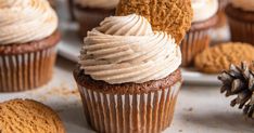 cupcakes with frosting and cookies on a white surface next to an orange pine cone