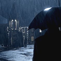 a person walking in the rain with an umbrella over their head and buildings behind them