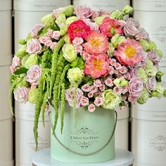 pink and green flowers are in a mint blue vase on a white table next to stacks of books