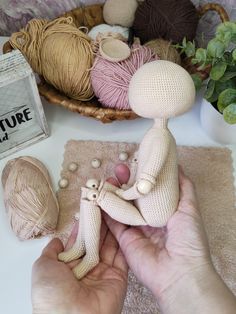 a person holding a small doll next to some balls of yarn