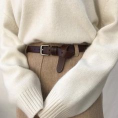 a person wearing a white sweater and brown pants with a belt around their waist,