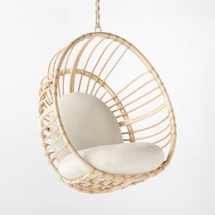 the hanging chair is made out of rattan and has a white cushion on it