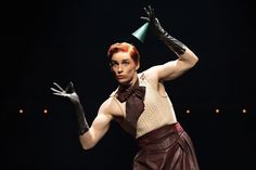 a woman with red hair and black gloves is dressed up as a mad hat, holding her hands in the air