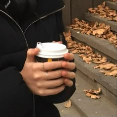 a person holding a coffee cup in front of some stairs with leaves on the ground