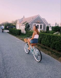 a woman riding a bike down a street next to houses and bushes on either side of the road