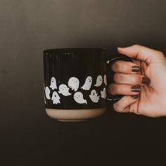 a woman's hand holding a black coffee mug with white ghost decals on it