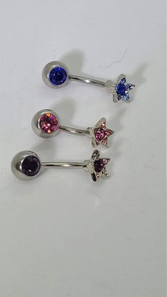 three piercings with different colored stones are shown on a white surface and one is in the shape of a butterfly