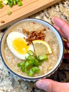 a person holding a bowl of oatmeal with an egg and sliced green onions