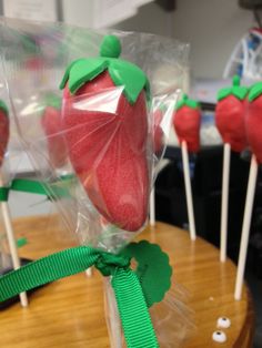 some strawberries are wrapped in plastic and sitting on top of sticks with green ribbons