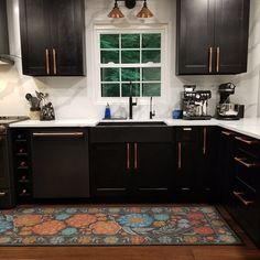 a kitchen with black cabinets and an area rug in front of the stove top oven