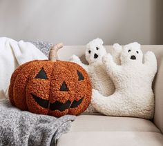 two pumpkins sitting on top of a couch with ghost pillows in front of them