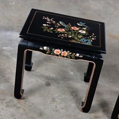 two small black tables with flowers painted on the top and one has gold trimmings