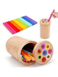 a child's hand is holding a wooden container with colored pencils in it