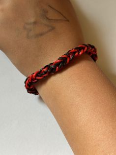 a person wearing a red and black braided bracelet on their left arm with a tattoo on it