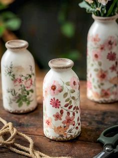 three vases with flowers painted on them are sitting on a table next to scissors