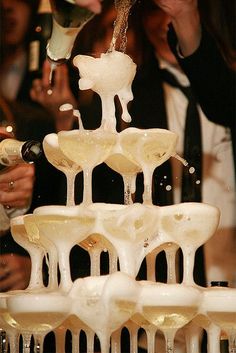 champagne being poured into wine glasses on top of a table with people standing around it