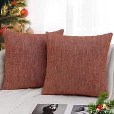 two orange pillows on a white couch near a christmas tree