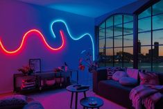 a living room filled with furniture and neon colored lights on the wall next to a large window