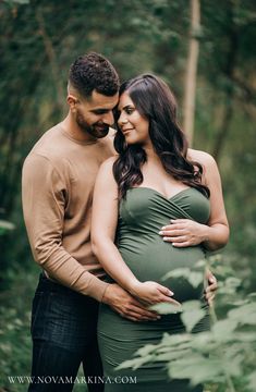 a pregnant couple cuddle in the woods