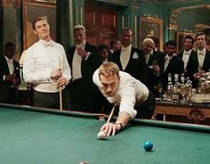 a man leaning over a pool table with a cue in his hand while others look on