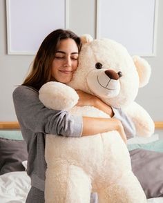 a woman hugging a large white teddy bear on top of a bed in a bedroom