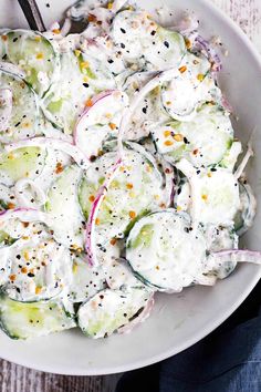 a white bowl filled with cucumber salad on top of a wooden table next to a spoon